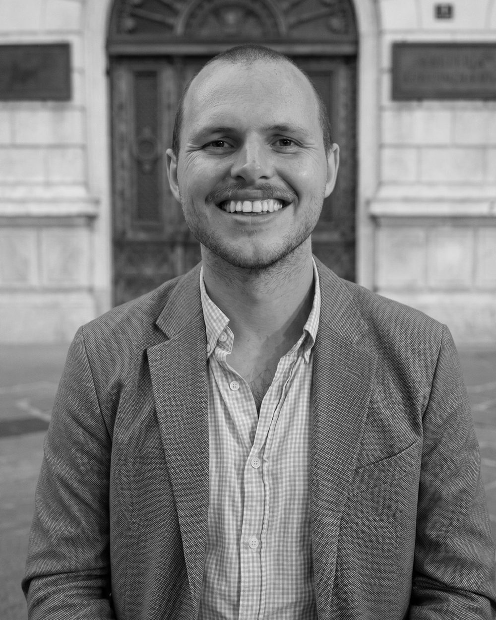 Portrait of Finn Clancy, smiling, in a grey blazer