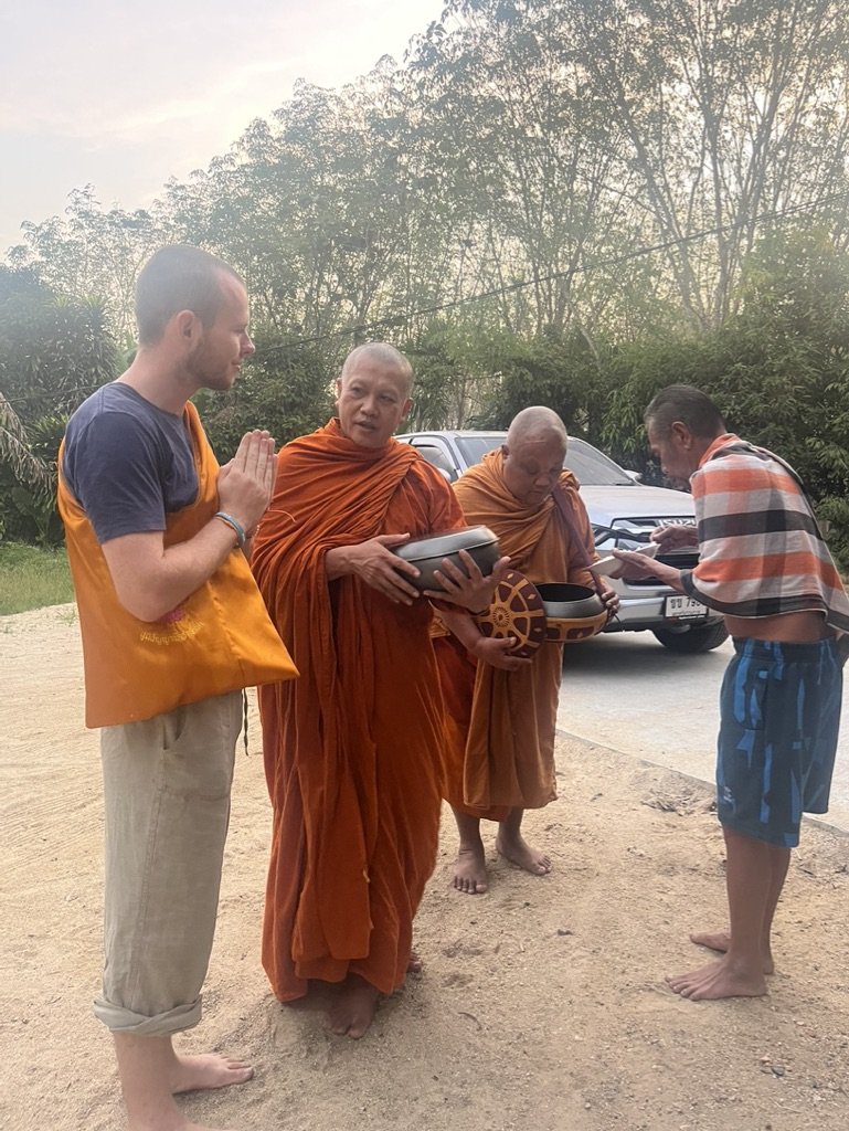 Finn standing with palms together as Buddhist monks receive alms on a rural road in Thailand